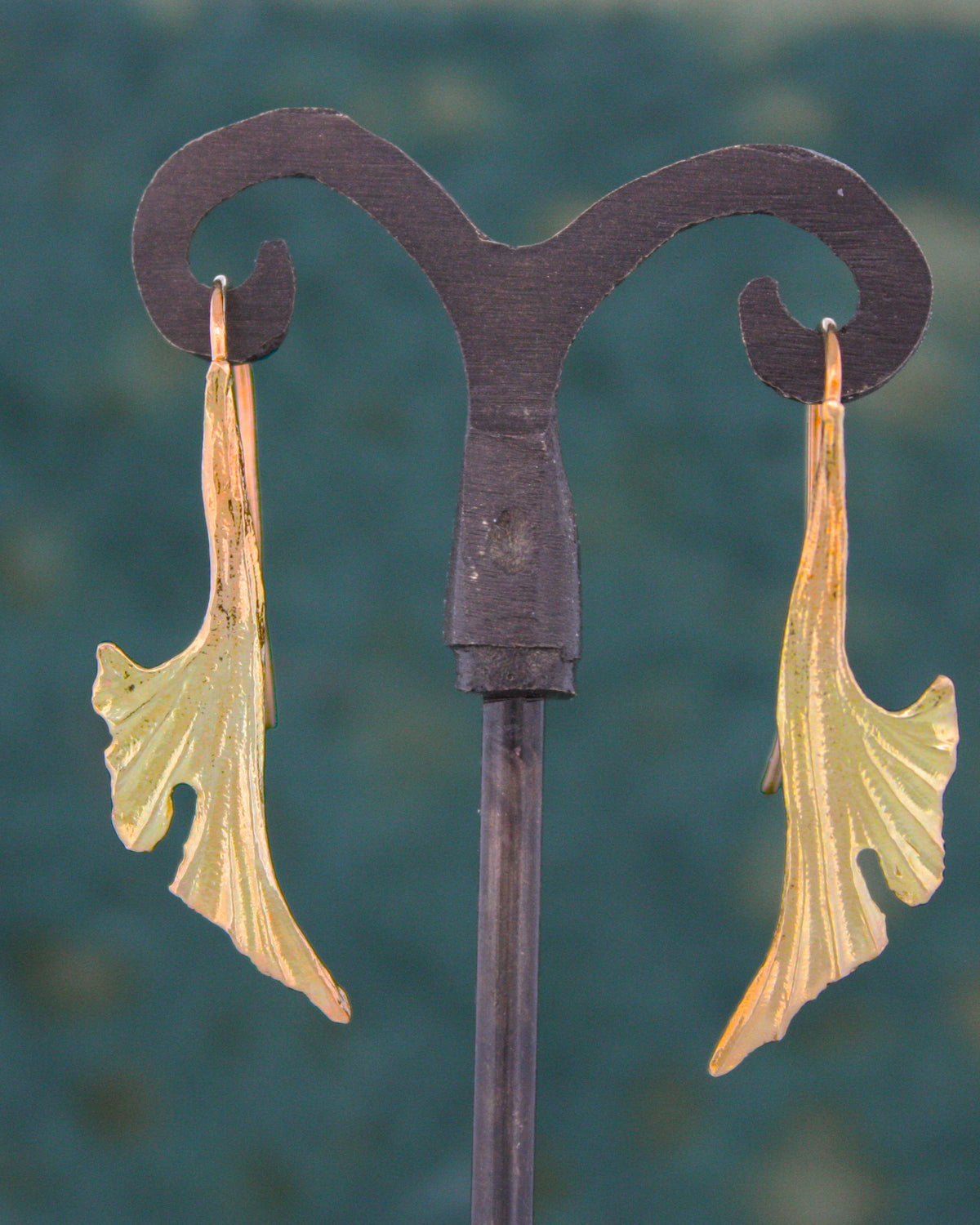 A pair of 18KY gold ginkgo leaf drop earrings displayed on a stand